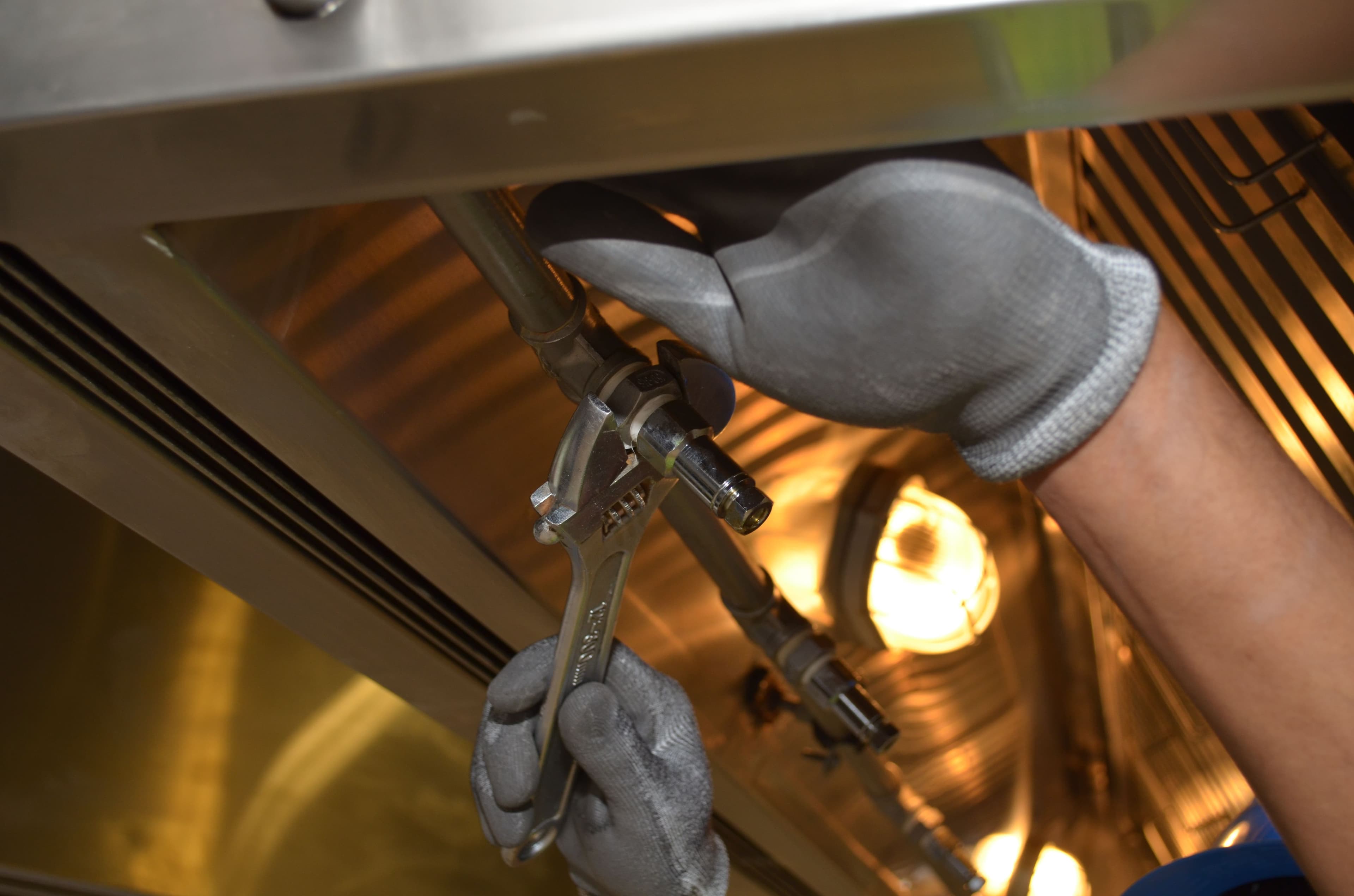 Gloved hands using pliers to connect a fixture's water line fittings