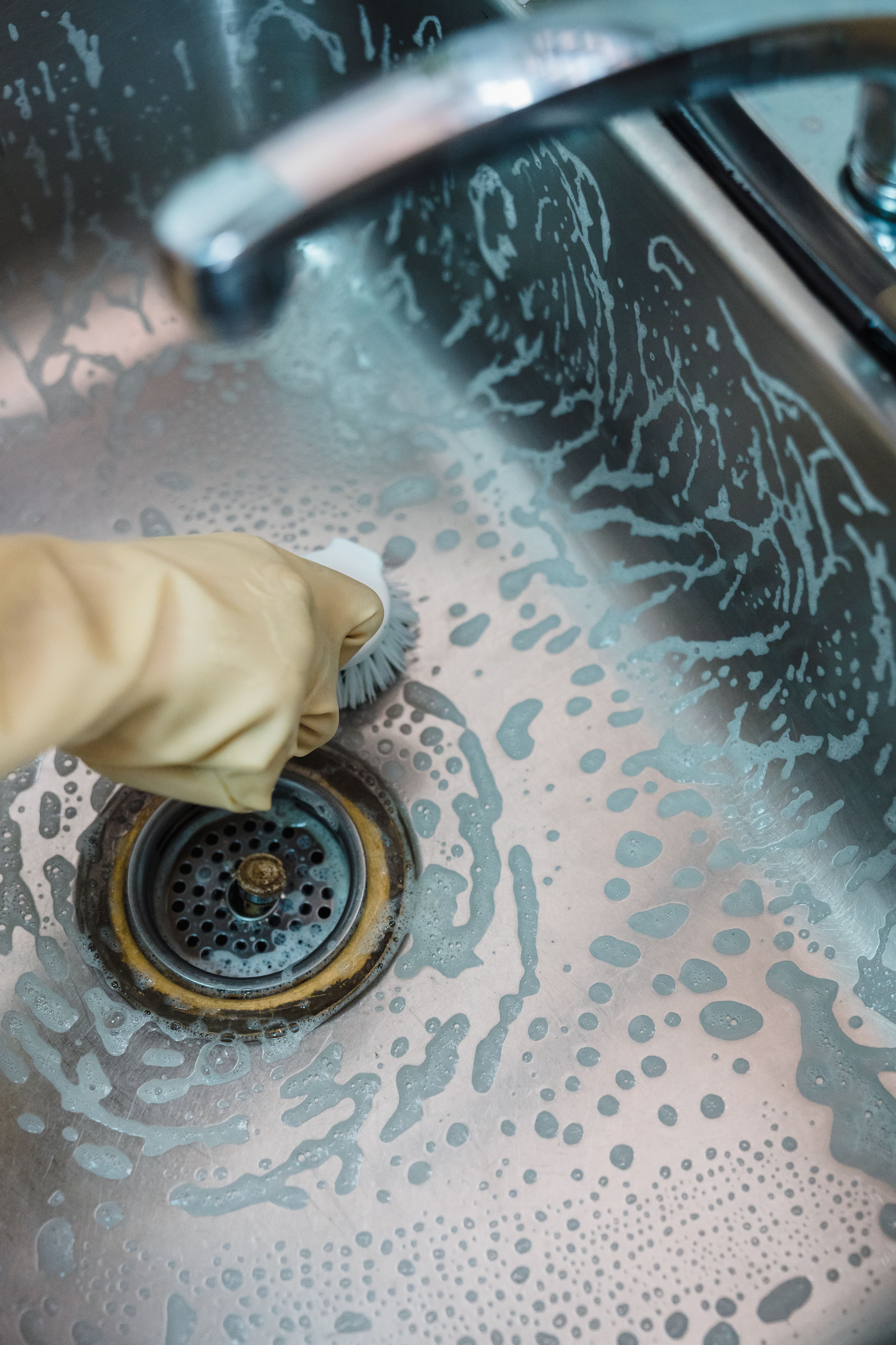 Gloved hand scrubbing and clearing a sink drain with a brush