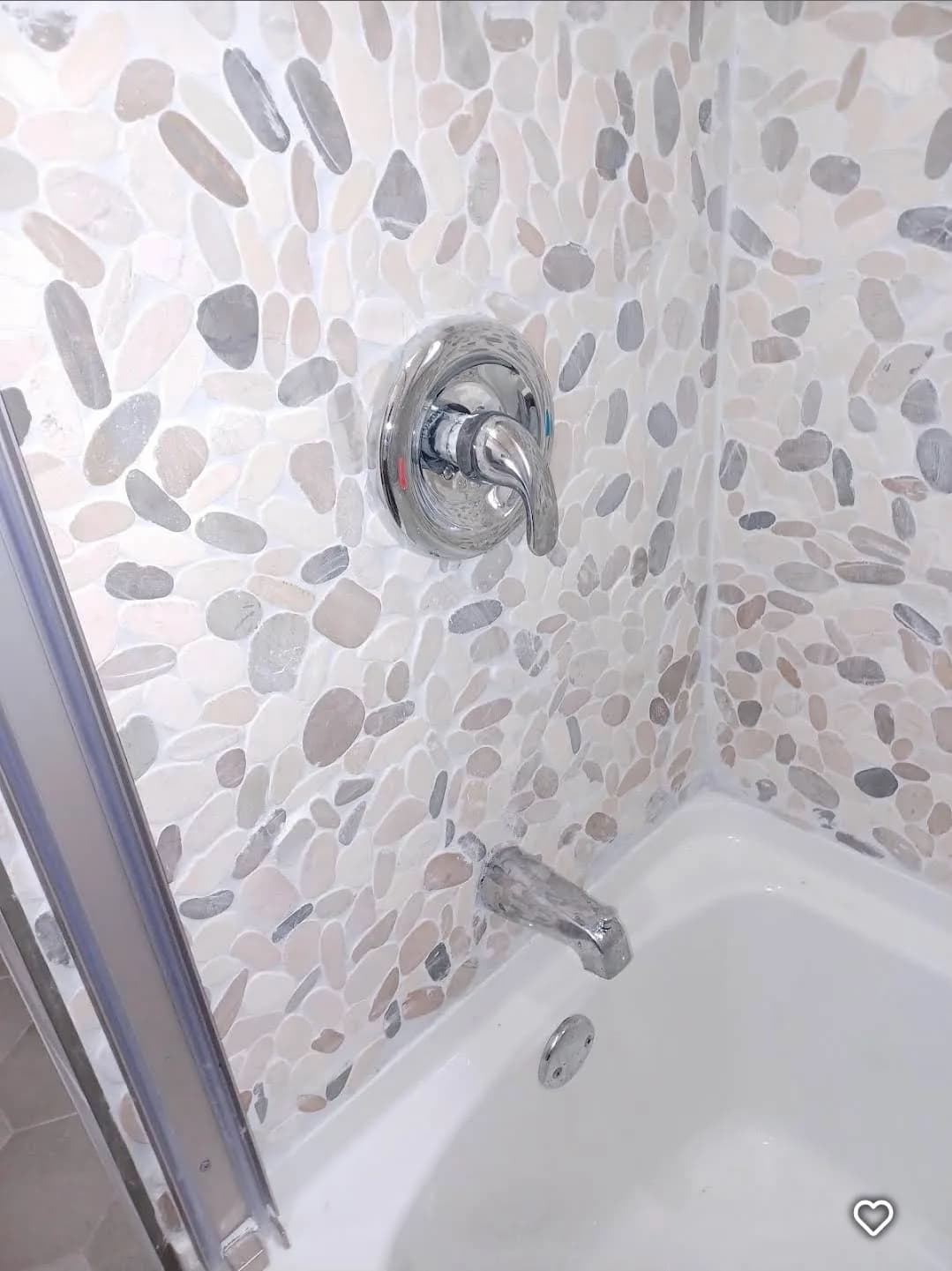 Completed shower with pebble tile surround, valve trim, and tub spout