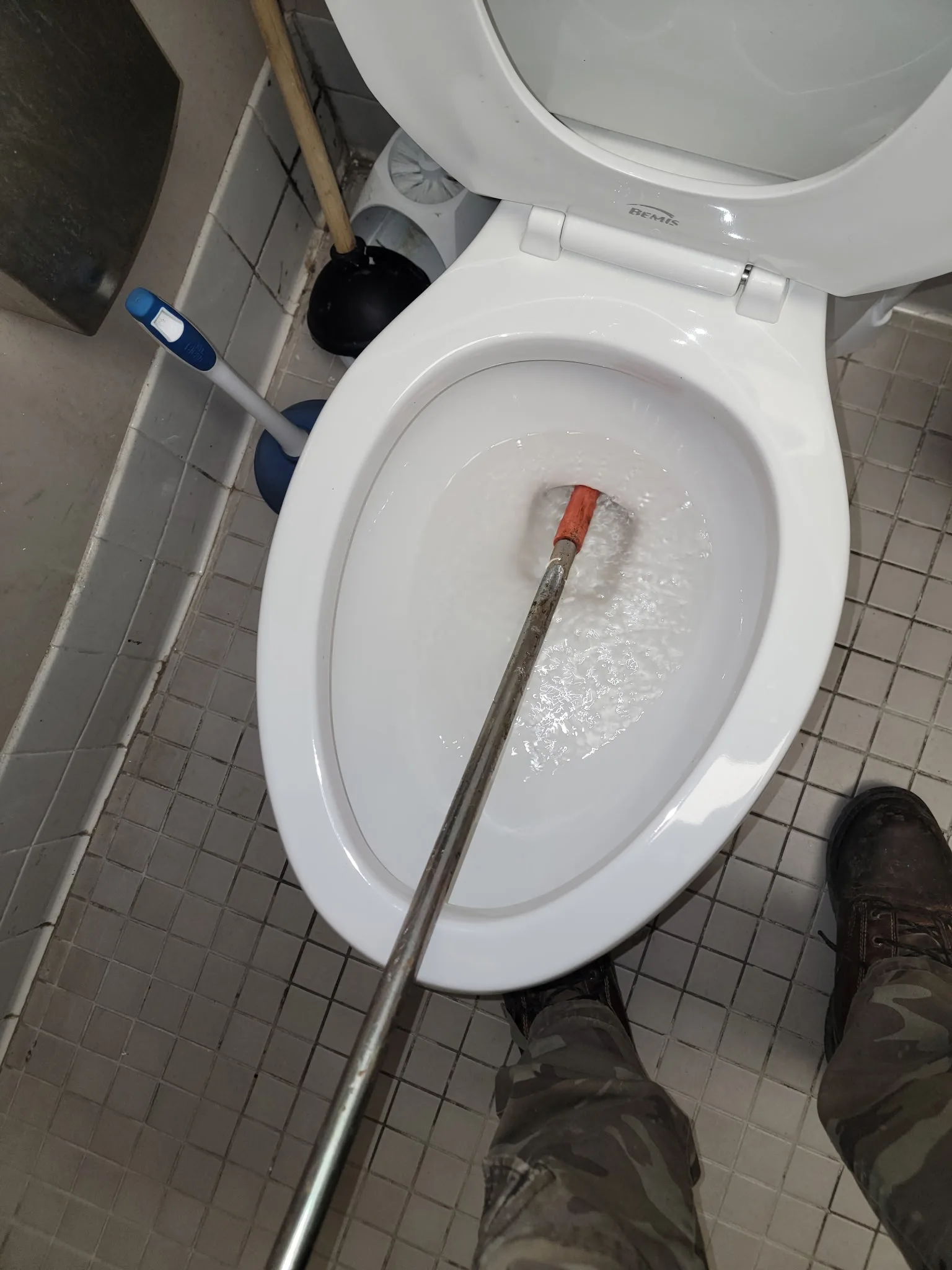 Toilet auger actively clearing a clogged toilet