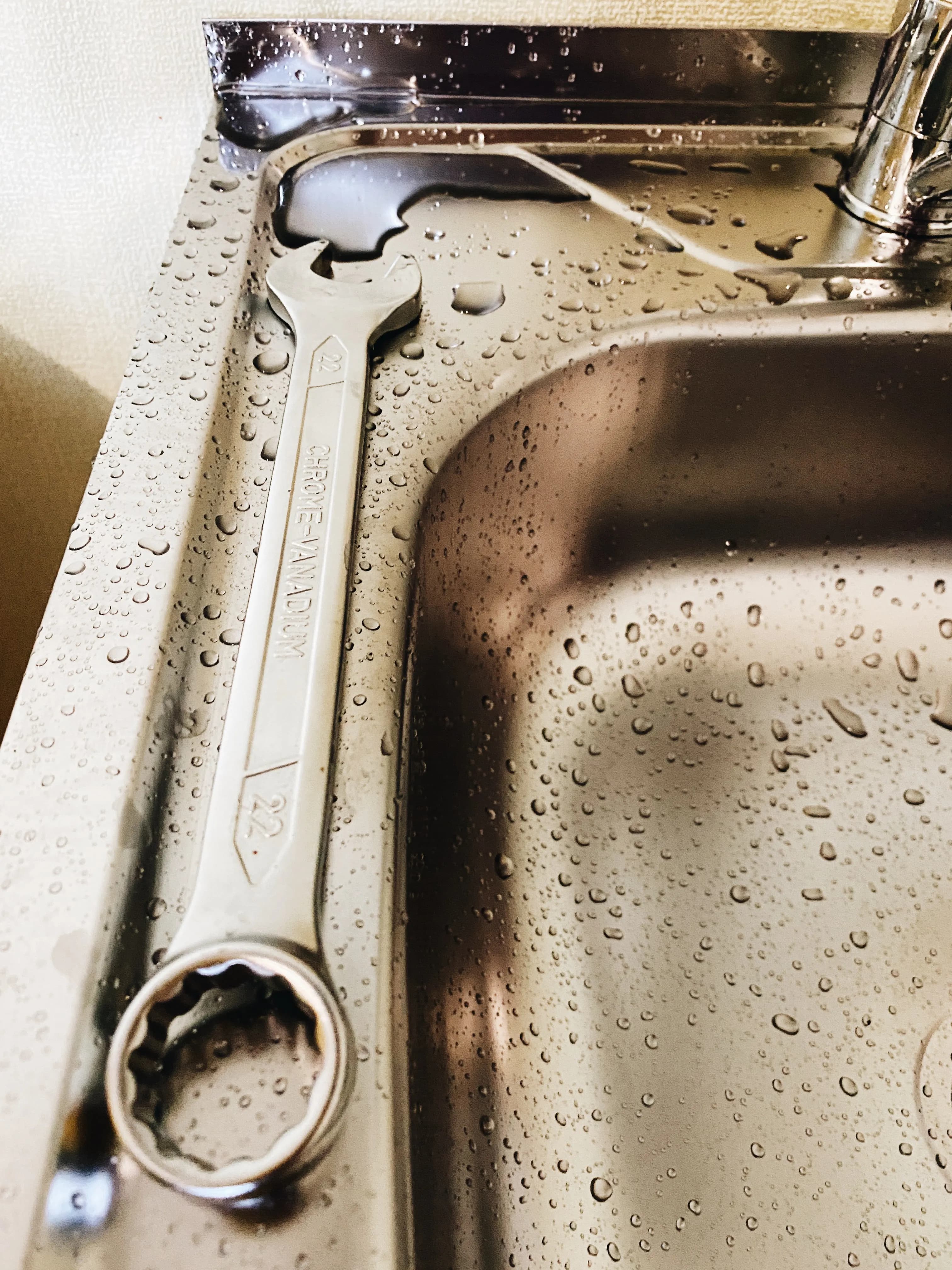 Wrench resting on a stainless steel sink during a plumbing job